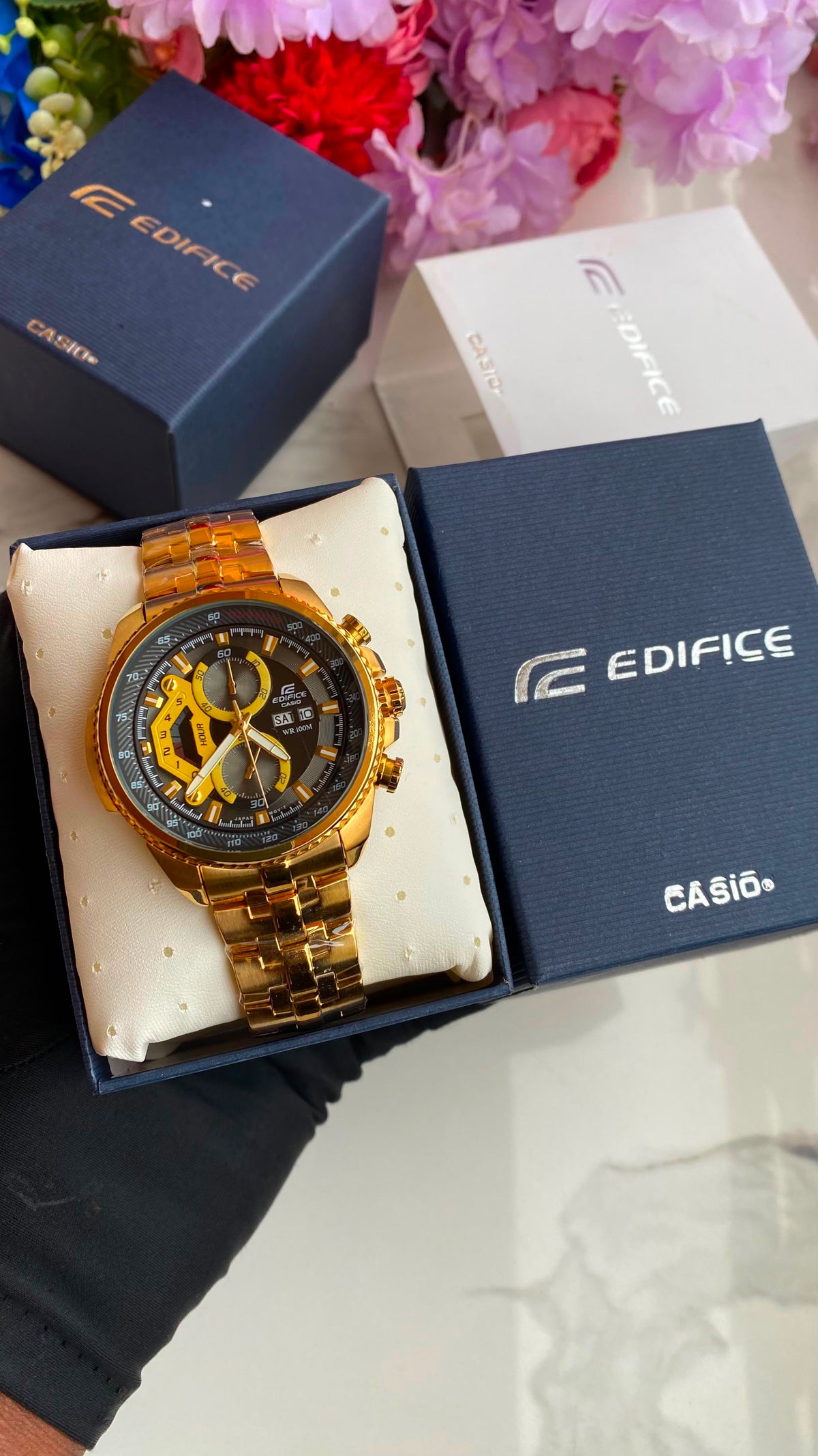 Gold-tone sport watch on a cushion beside watch boxes.